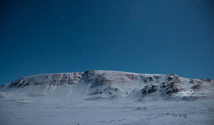 Snöklädda berg endast upplyst av månen en stärnklar natt, Island