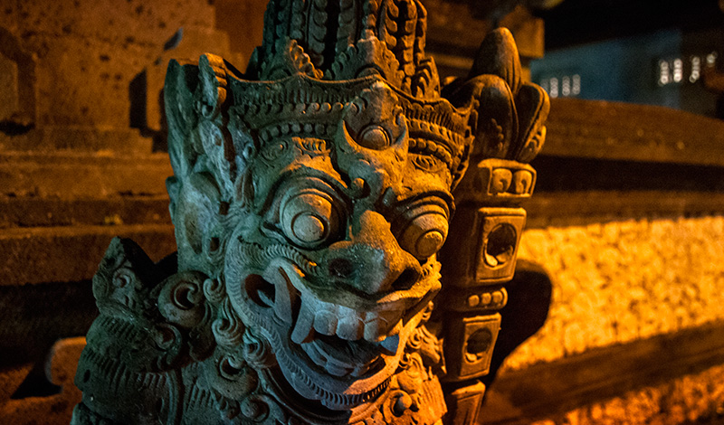 Demon staty i kvällsbelysning längs Sanur strandpromenad, Bali